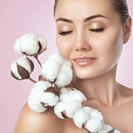 Portrait of a beautiful woman with beautiful make-up, with cotton flower in her hand on a pink background. Cosmetology and professional skin care.