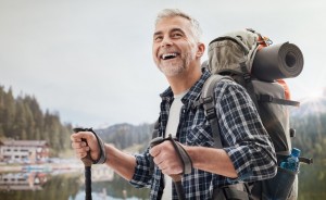 Confident mature man doing nordic walking on the mountains, he is using trekking poles and carrying a backpack, freedom and sports concept